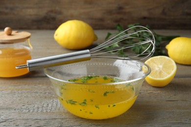 Whisk and bowl with lemon sauce on wooden table. Delicious salad dressing