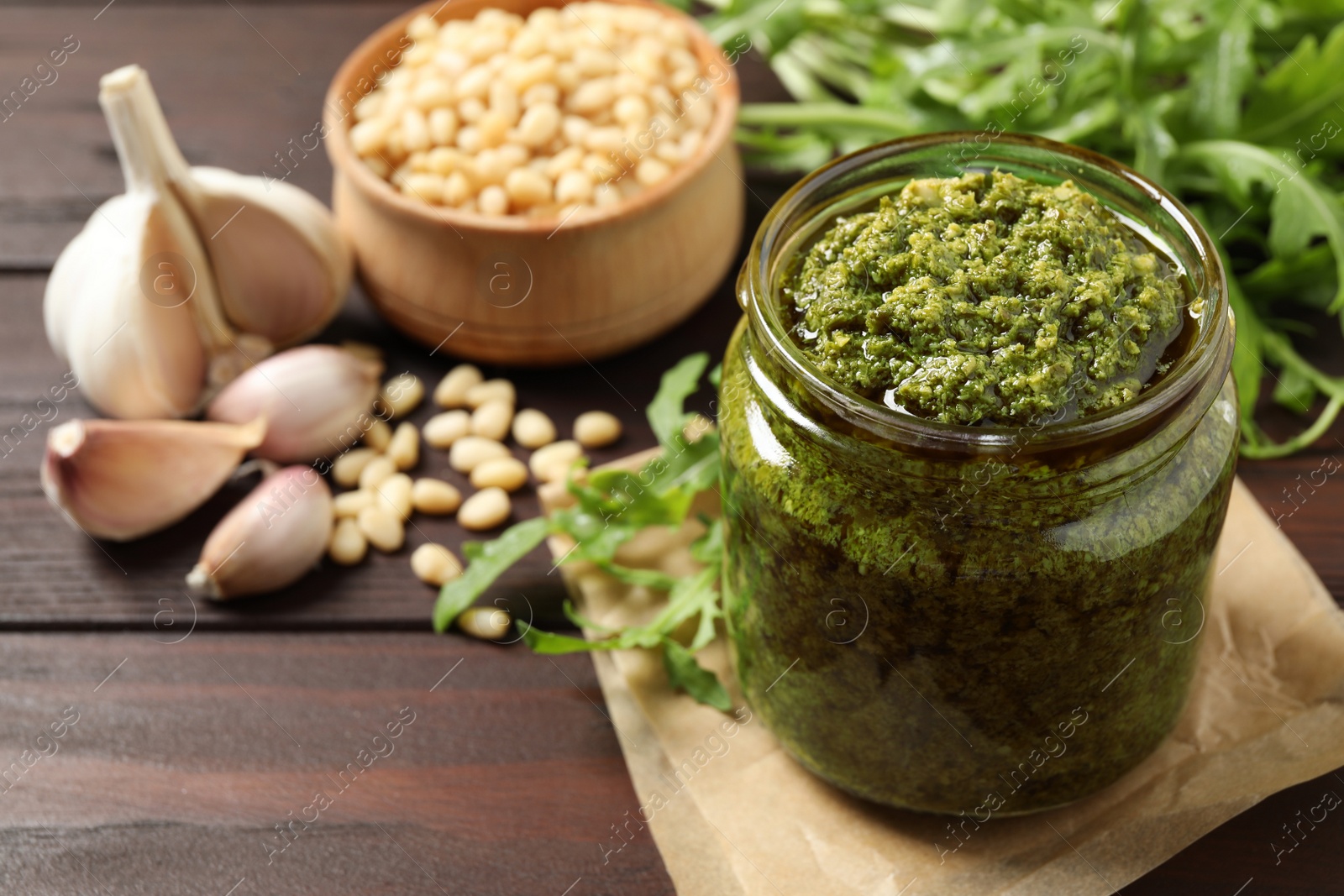 Photo of Jar of tasty arugula pesto and ingredients on wooden table. Space for text