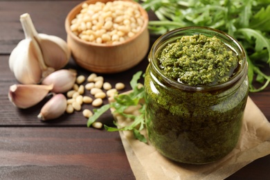 Photo of Jar of tasty arugula pesto and ingredients on wooden table. Space for text