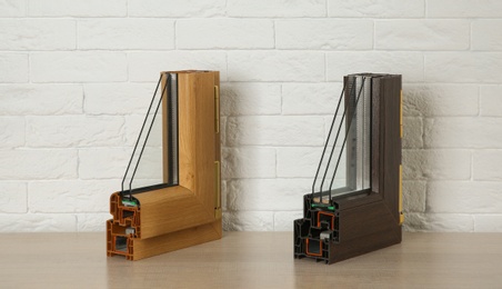 Photo of Samples of modern window profiles on table against brick wall. Installation service