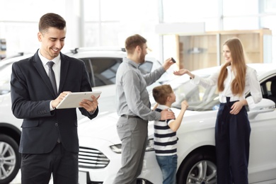 Photo of Salesman with tablet and young family in car salon