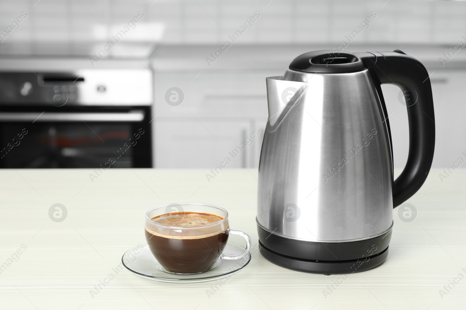 Photo of Modern electric kettle and cup of coffee on white wooden table in kitchen. Space for text