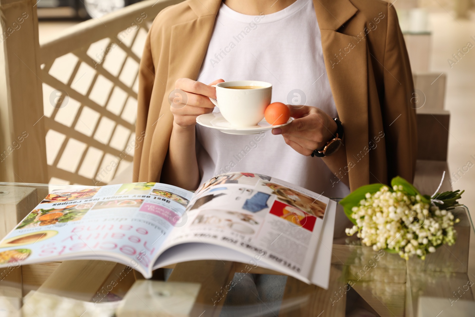 Photo of Woman with cup of coffee reading magazine at outdoor cafe in morning, closeup