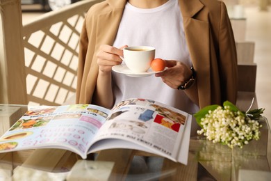 Woman with cup of coffee reading magazine at outdoor cafe in morning, closeup