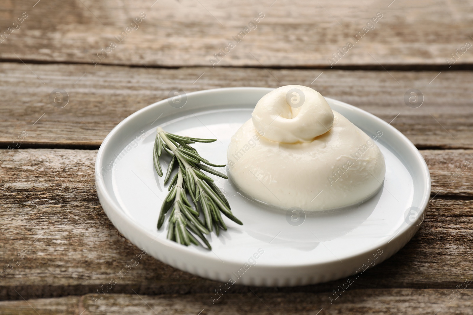 Photo of Delicious burrata cheese with rosemary on wooden table