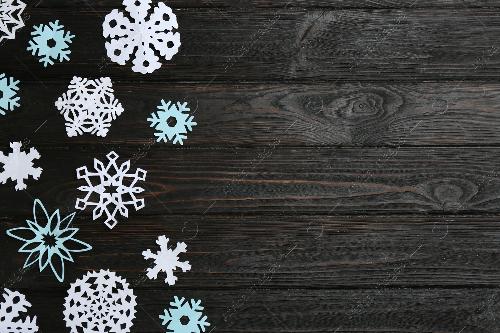 Photo of Different paper snowflakes on black wooden table, flat lay. Space for text