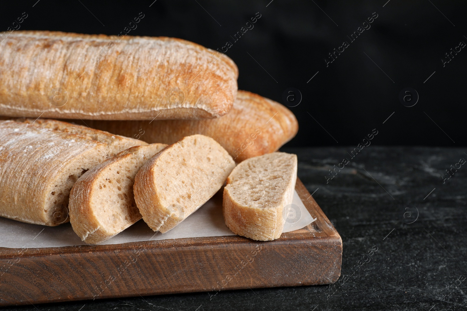 Photo of Wooden board with delicious ciabattas on black table
