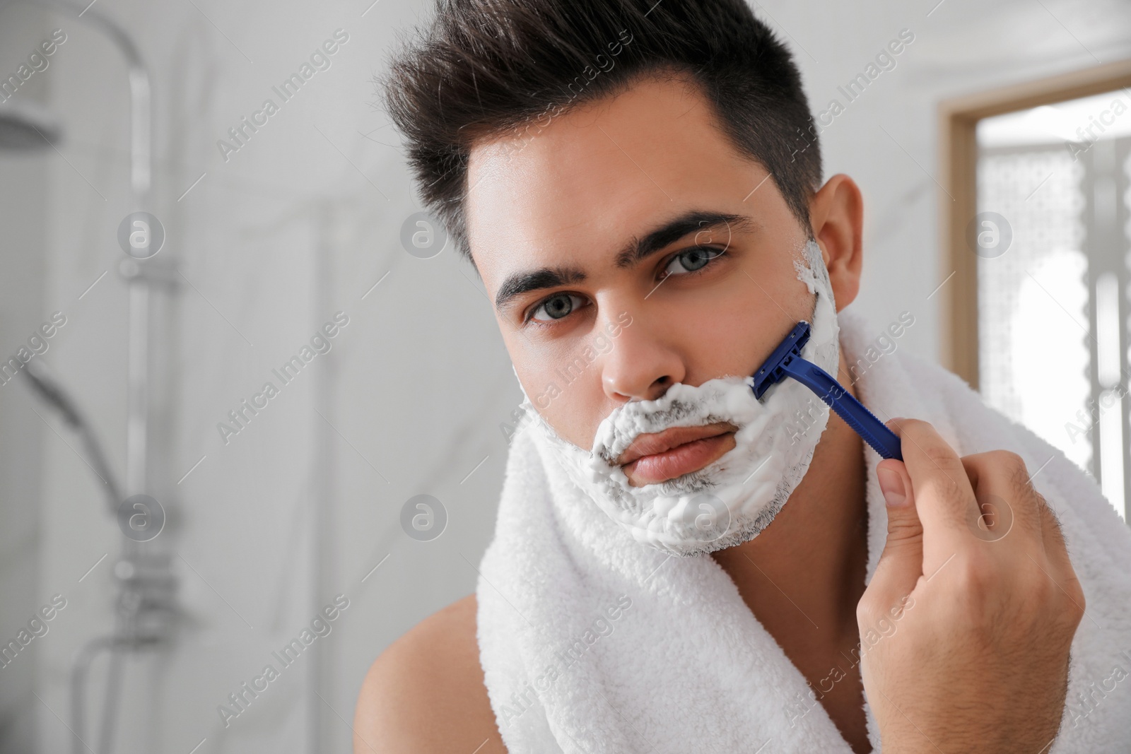 Photo of Handsome young man shaving with razor in bathroom, space for text