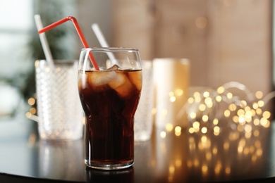 Photo of Glass of cold cola and fairy lights on table. Space for text