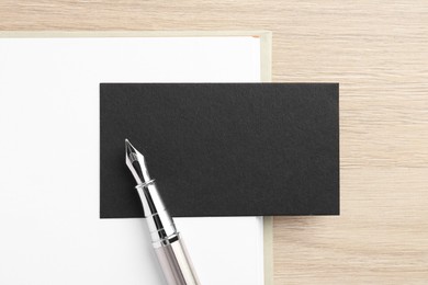 Photo of Blank black business card, fountain pen and notebook on wooden table, top view. Mockup for design