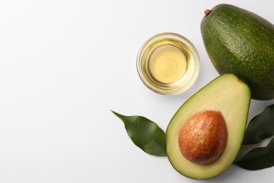 Photo of Cooking oil in bowl and fresh avocados on white background, flat lay. Space for text