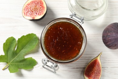 Photo of Glass jar with tasty sweet jam, green leaf and fresh figs on white wooden table, flat lay