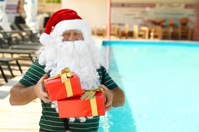 Photo of Authentic Santa Claus with gift boxes near pool at resort