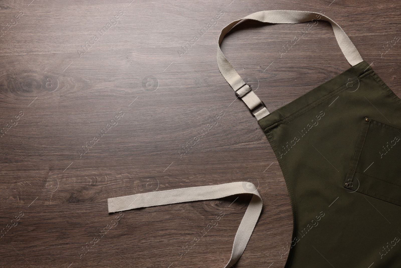 Photo of Stylish dark olive apron on wooden table, top view. Mockup for design