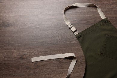 Stylish dark olive apron on wooden table, top view. Mockup for design