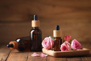 Bottles of essential rose oil and flowers on wooden table