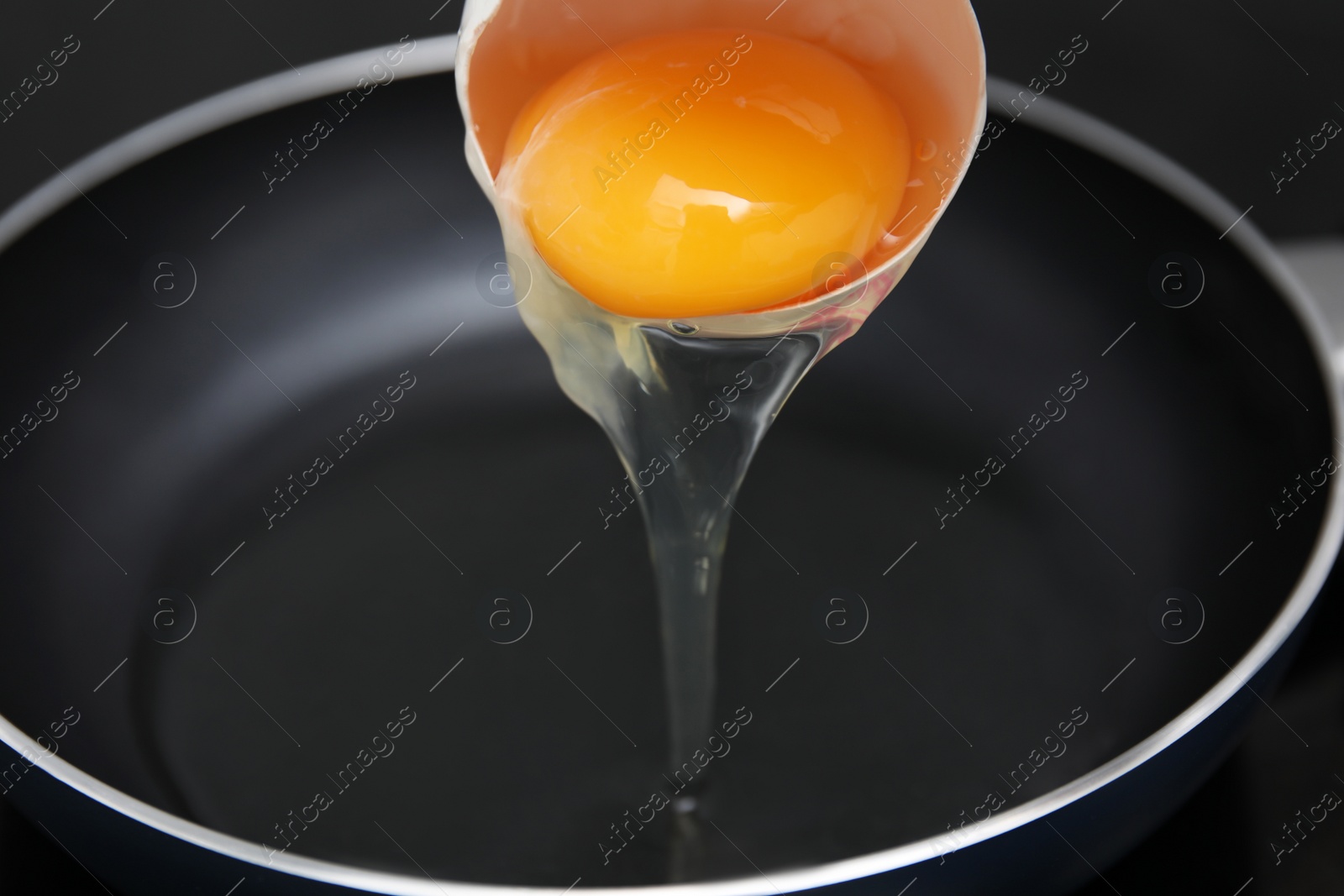 Photo of Adding raw egg into frying pan, closeup