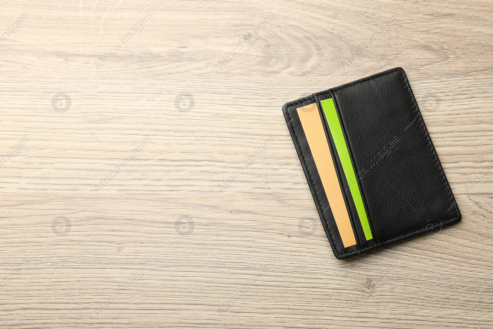 Photo of Leather business card holder with colorful cards on wooden table, top view. Space for text