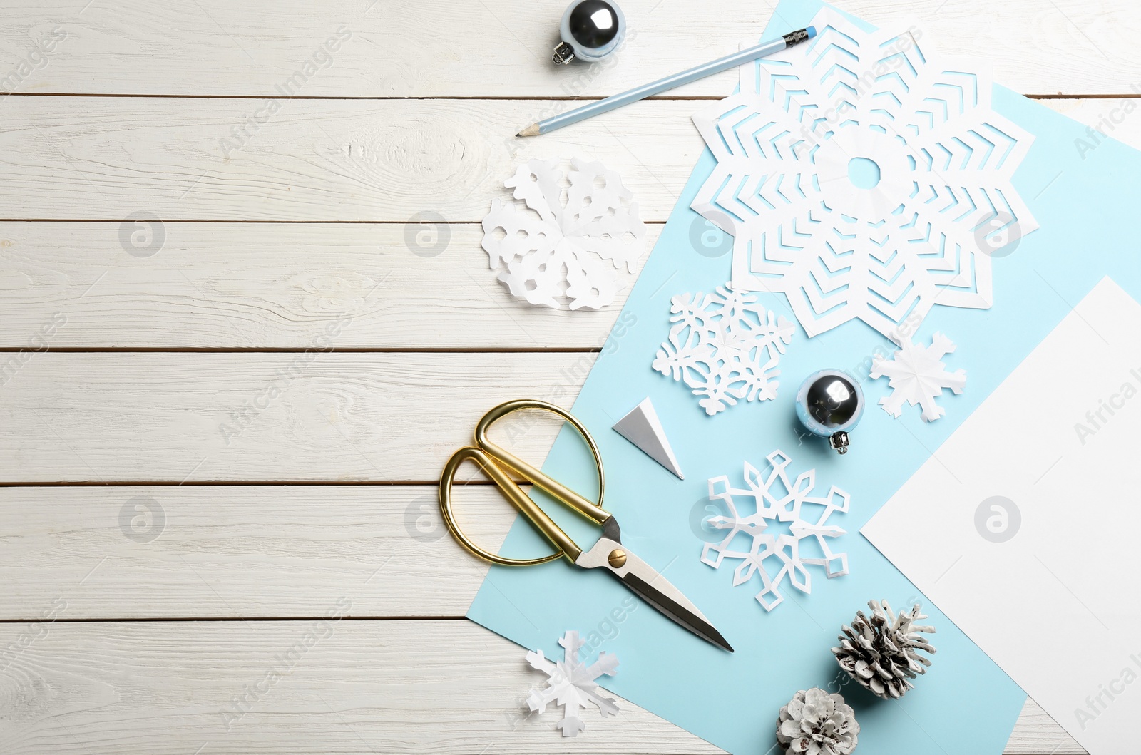 Photo of Flat lay composition with paper snowflakes, scissors and Christmas decoration on white wooden background, space for text