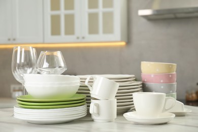 Photo of Clean plates, bowls, cups and glasses on white marble table in kitchen