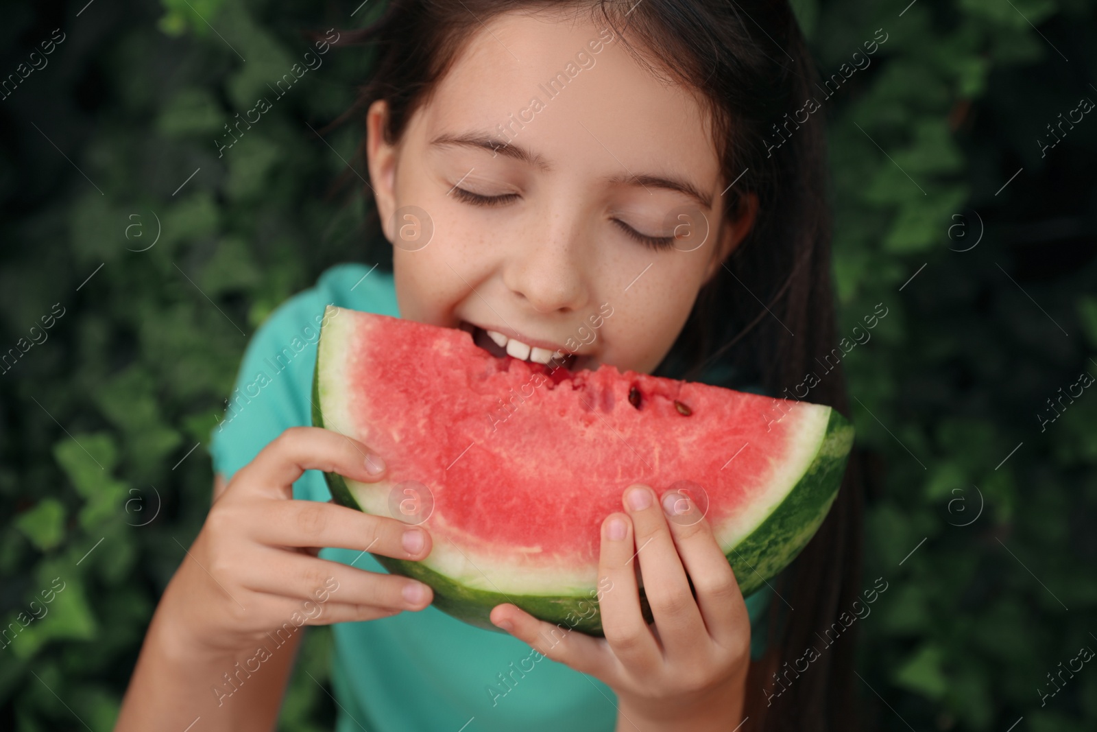 Photo of Cute little girl eating watermelon outdoors on sunny day, closeup