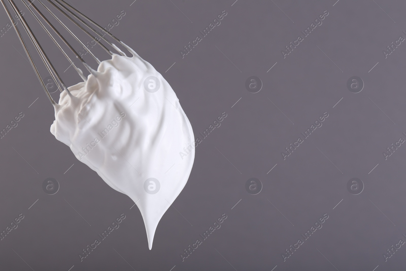 Photo of Whisk with whipped cream on grey background. Space for text