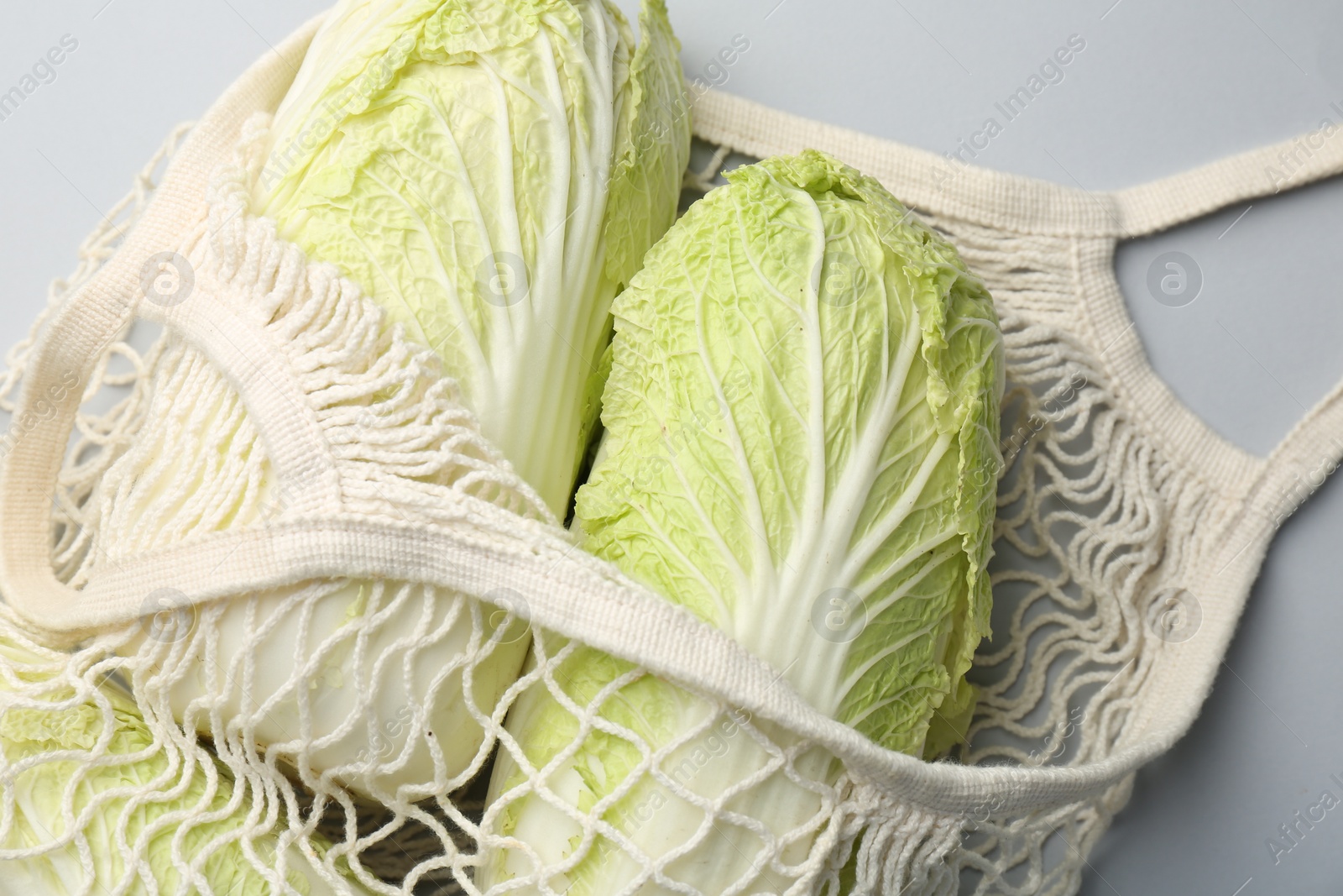 Photo of Fresh Chinese cabbages in string bag on light background, top view