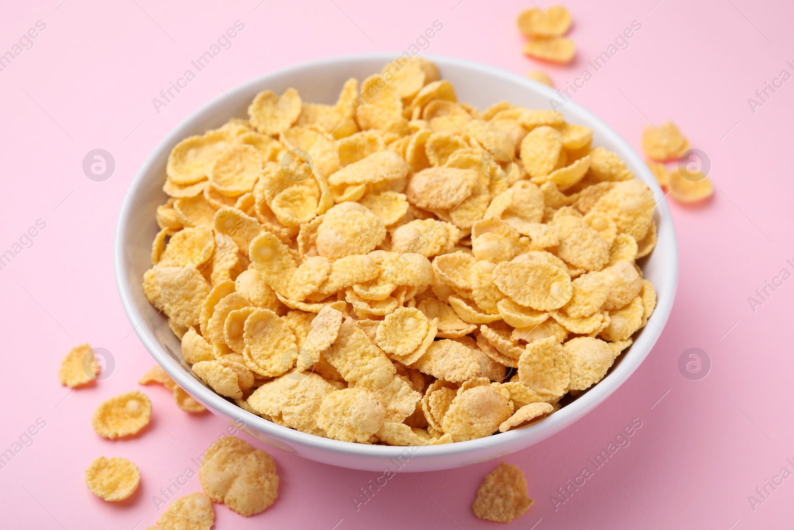 Photo of Breakfast cereal. Tasty corn flakes in bowl on pink table, closeup