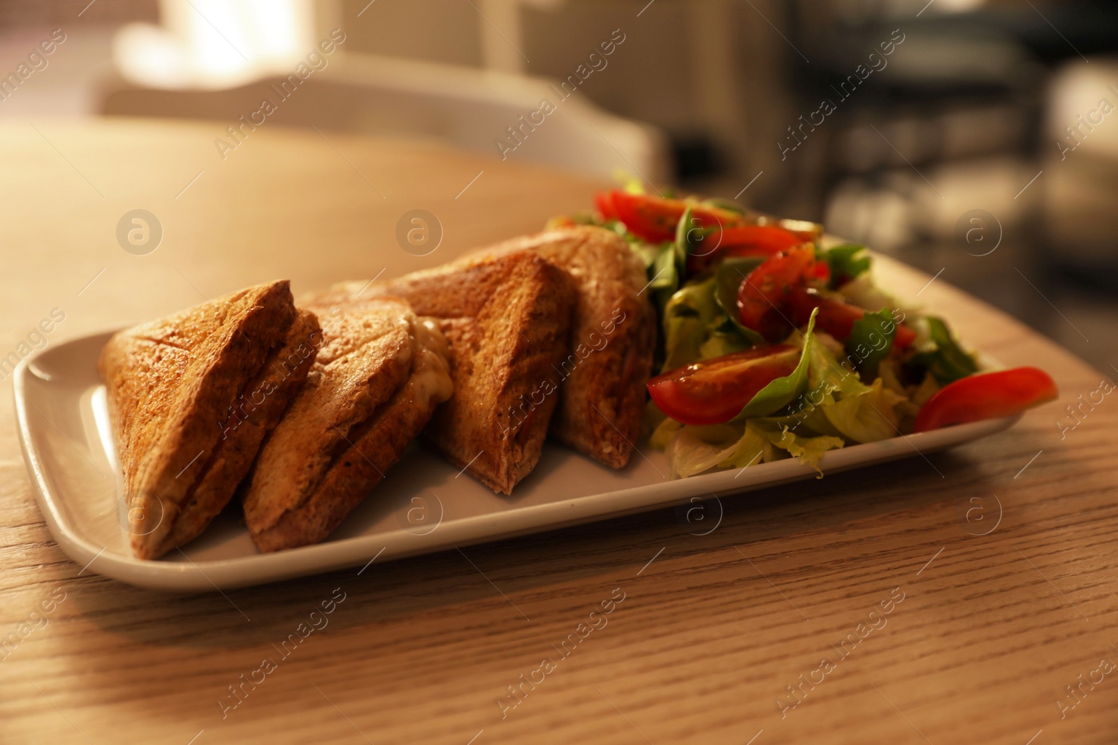 Photo of Plate of delicious toasts and salad on wooden table in cafe, closeup