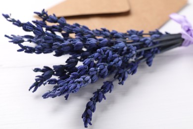 Photo of Bouquet of beautiful preserved lavender flowers and envelope on white wooden table, closeup