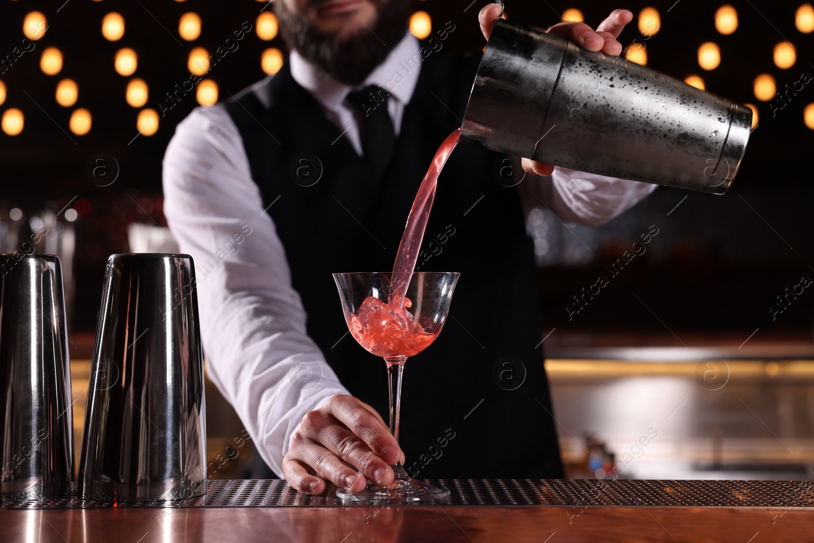 Photo of Bartender preparing fresh alcoholic cocktail in martini glass at bar counter, closeup