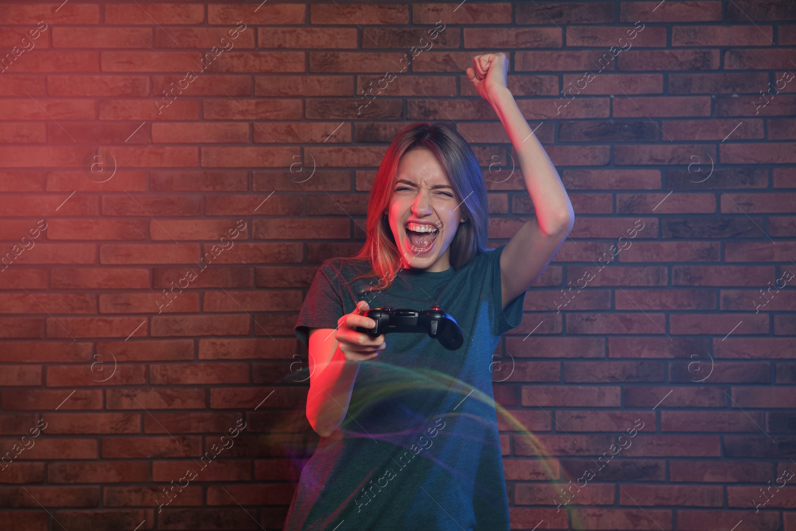 Photo of Emotional young woman playing video games with controller near brick wall