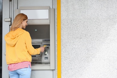 Photo of Beautiful woman using cash machine outdoors. Space for text