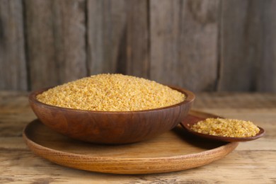 Photo of Bowl and spoon with uncooked bulgur on wooden table