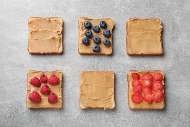 Photo of Tasty peanut butter sandwiches with fresh berries on gray table, flat lay