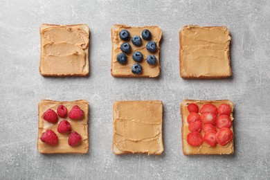 Tasty peanut butter sandwiches with fresh berries on gray table, flat lay