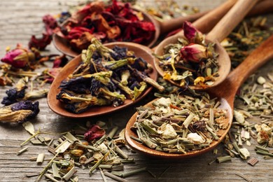 Spoons with different teas on wooden table, closeup