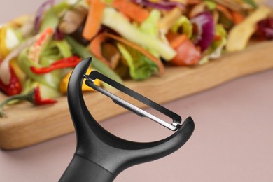 Photo of Peels of fresh vegetables and peeler on dusty pink background, closeup