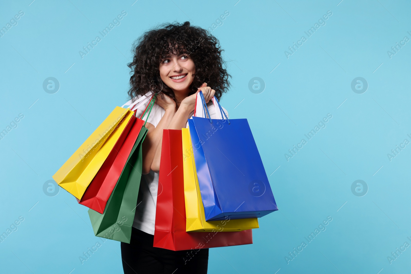 Photo of Happy young woman with shopping bags on light blue background