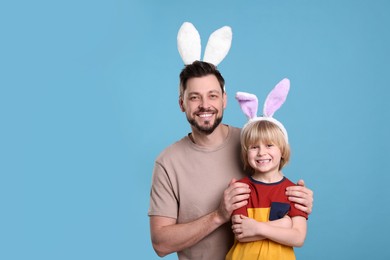 Photo of Father and son in bunny ears headbands having fun on turquoise background, space for text. Easter celebration