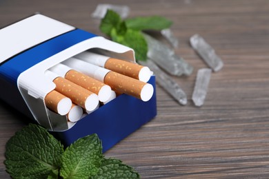 Photo of Pack of cigarettes, menthol crystals and mint on wooden table, closeup. Space for text