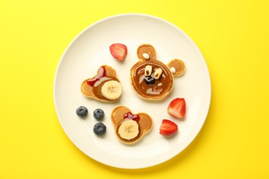 Creative serving for kids. Plate with cute bears made of pancakes, berries, banana and chocolate paste on yellow background, top view