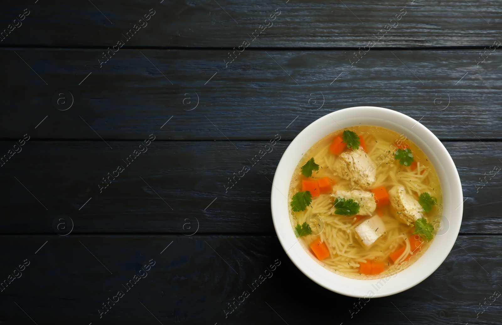 Photo of Homemade chicken soup in dish on wooden background, top view with space for text