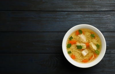 Homemade chicken soup in dish on wooden background, top view with space for text