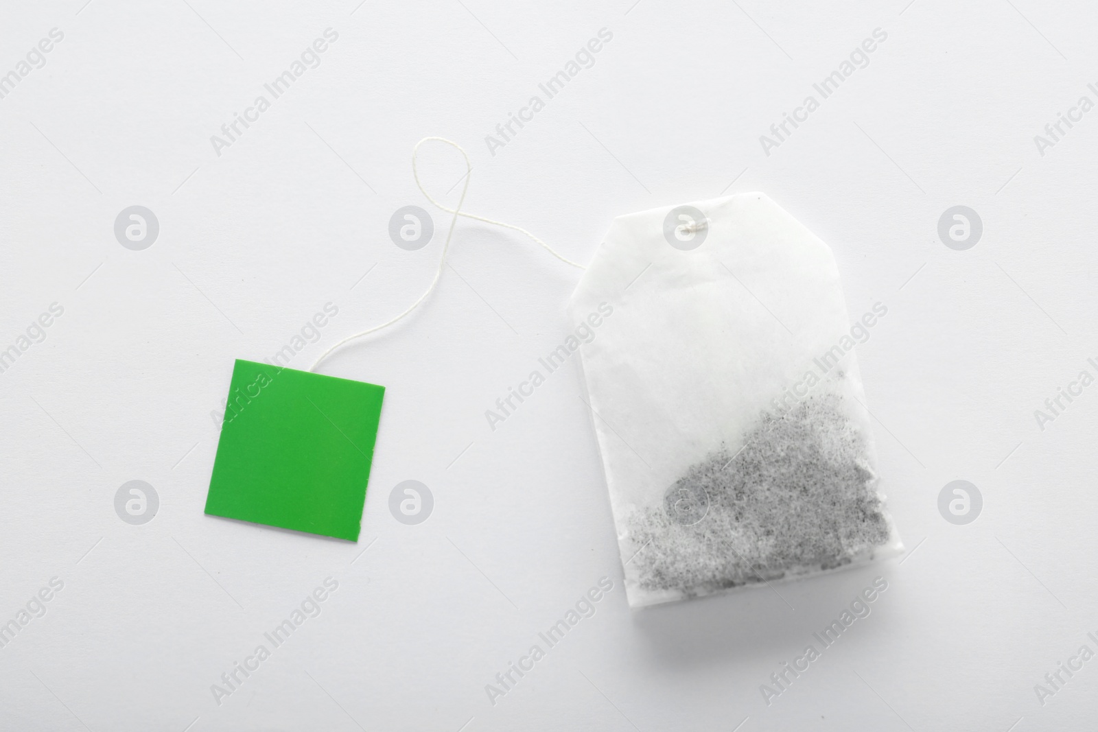 Photo of Unused tea bag with tag on white background, top view. Space for text