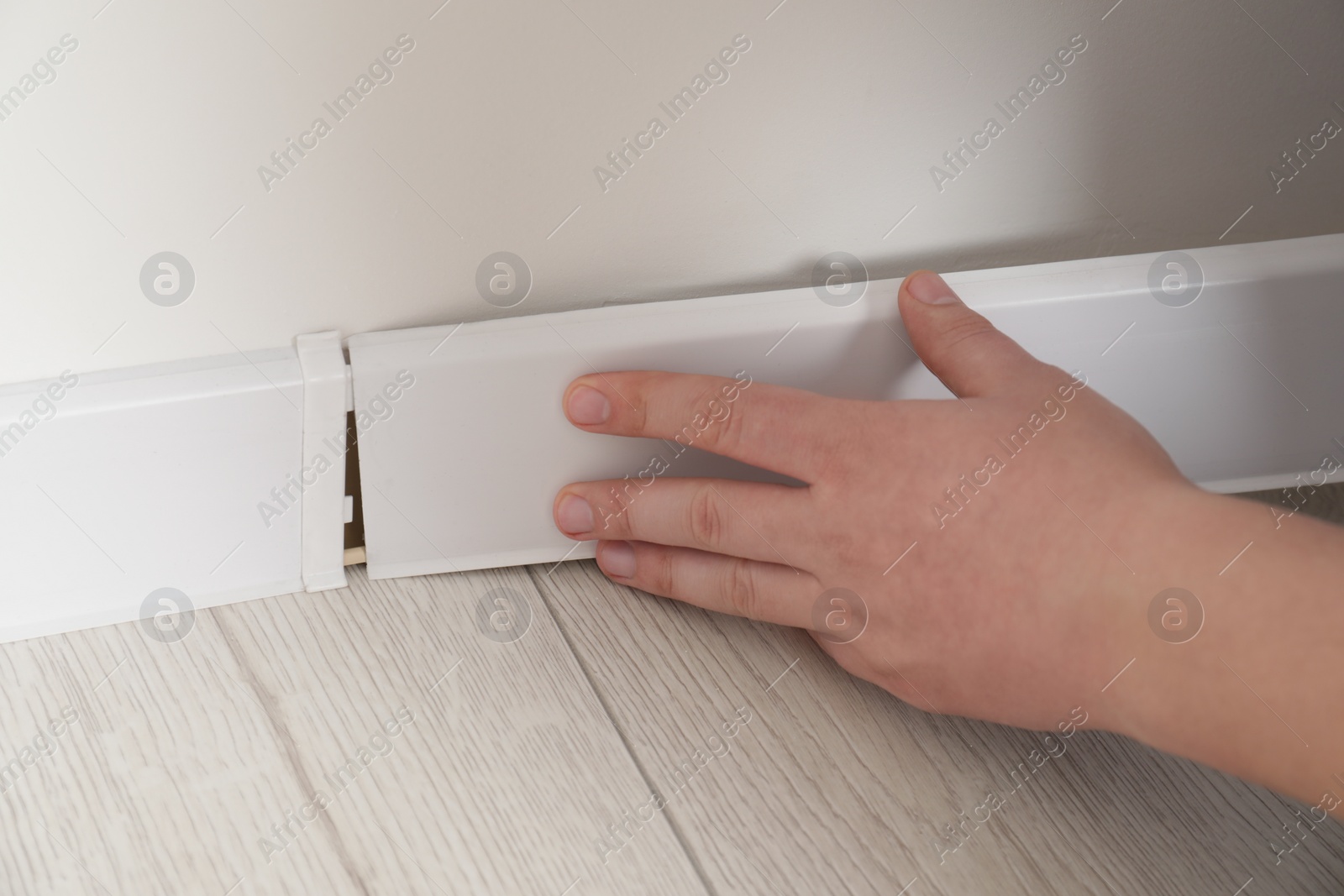 Photo of Man installing plinth on laminated floor in room, closeup