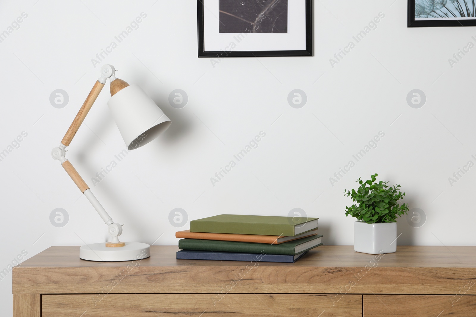 Photo of Desk lamp, books and houseplant on wooden chest of drawers indoors