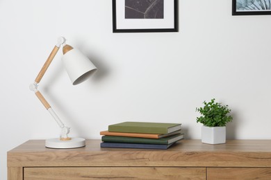 Photo of Desk lamp, books and houseplant on wooden chest of drawers indoors
