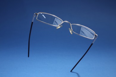 Photo of Stylish pair of glasses with metal frame on blue background