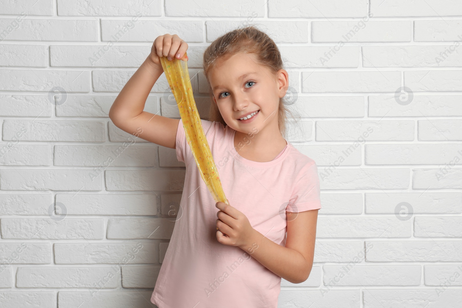 Photo of Little girl with slime near white brick wall